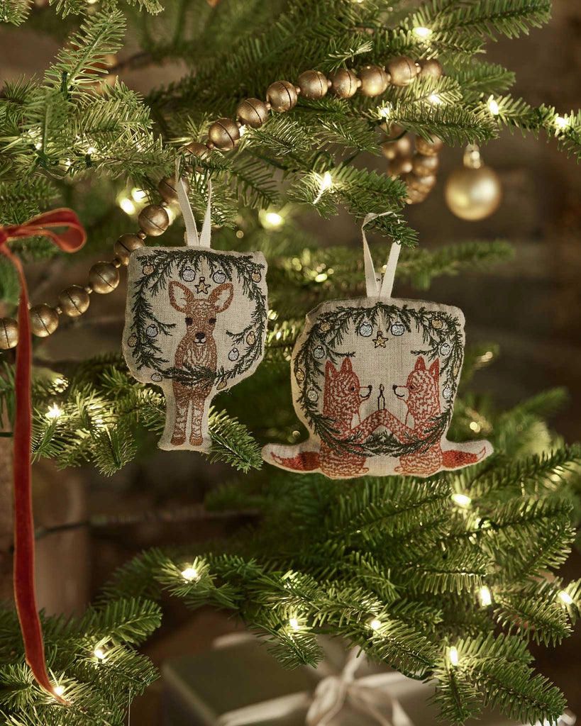 The Coral & Tusk Togetherness Deer Ornament hangs on a Christmas tree decorated with string lights, gold beads, and festive accents, beautifully capturing the spirit of togetherness.