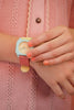 Wearing coral nail polish and a pink scalloped-edge knit top with a brown button, someone touches their Mini Kyomo Watch - Bubble Gum.