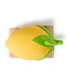 A yellow, lemon-shaped Lou The Lemon Baby Car made of natural rubber with green leaves sits atop a small rectangular wooden block, viewed from above against a white background.
