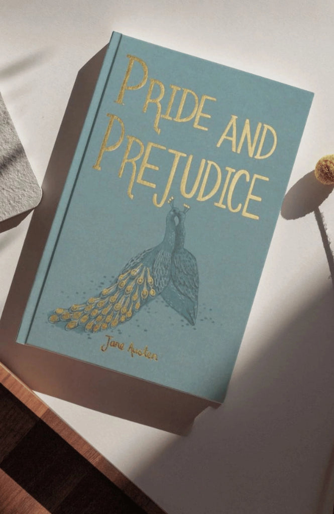 A collector’s edition hardcover of "Pride and Prejudice" by Austen, with gold lettering and a peacock design, rests on a sunlit light surface.
