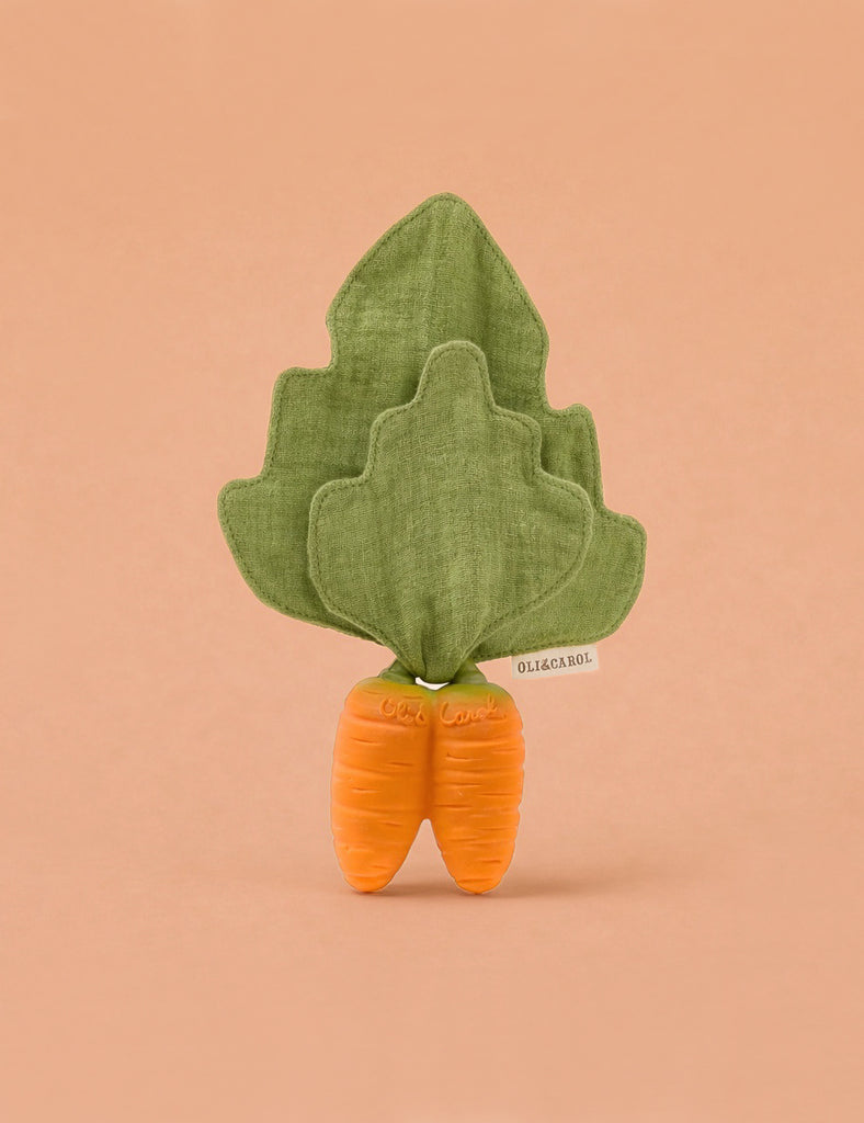 Cathy the Carrot Mini DouDou Teether is a soft toy with two orange roots and green leafy fabric on top—perfect for babies to support sensory development. Shown standing upright against a plain peach background.