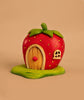 The Bumbu Handmade Wooden Strawberry House, shaped like a strawberry with a wooden door, window, green leaves, and base, is perfect for small world play. Ships in one week. Set against a plain beige background.