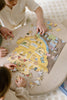 Two children assemble the Honeycomb Cafe 200 Piece Puzzle, featuring a charming house scene with matte textured pieces spread across a light wooden table.