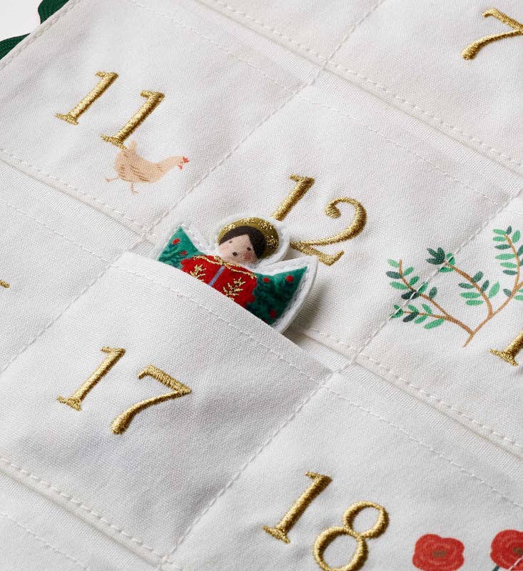 A Nativity Embroidered Hanging Advent Calendar with embroidered numbers and seasonal icons, featuring a small angel figurine tucked into the pocket for day twelve.