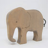 The Handmade Wooden Elephant is a minimalist figurine crafted from sustainable hardwood, with a curved trunk, small eye, wavy mouth, black cord tail, and set against a plain white background.