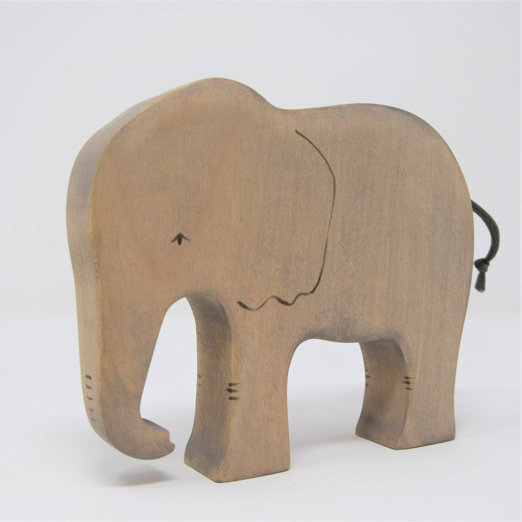 The Handmade Wooden Elephant is a minimalist figurine crafted from sustainable hardwood, with a curved trunk, small eye, wavy mouth, black cord tail, and set against a plain white background.
