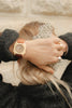A person with blonde hair in a low ponytail holds a white scrunchie with black dots, wearing the Mini Kyomo Watch - Cherry Bomb, multiple rings, and a dark textured sweater.