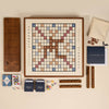 The 3-in-1 Game Collection features a Scrabble board with letter tiles and racks, Trivial Pursuit cards, playing cards, dice, colored tokens, and a classic wooden cribbage board—all the essentials for game night.