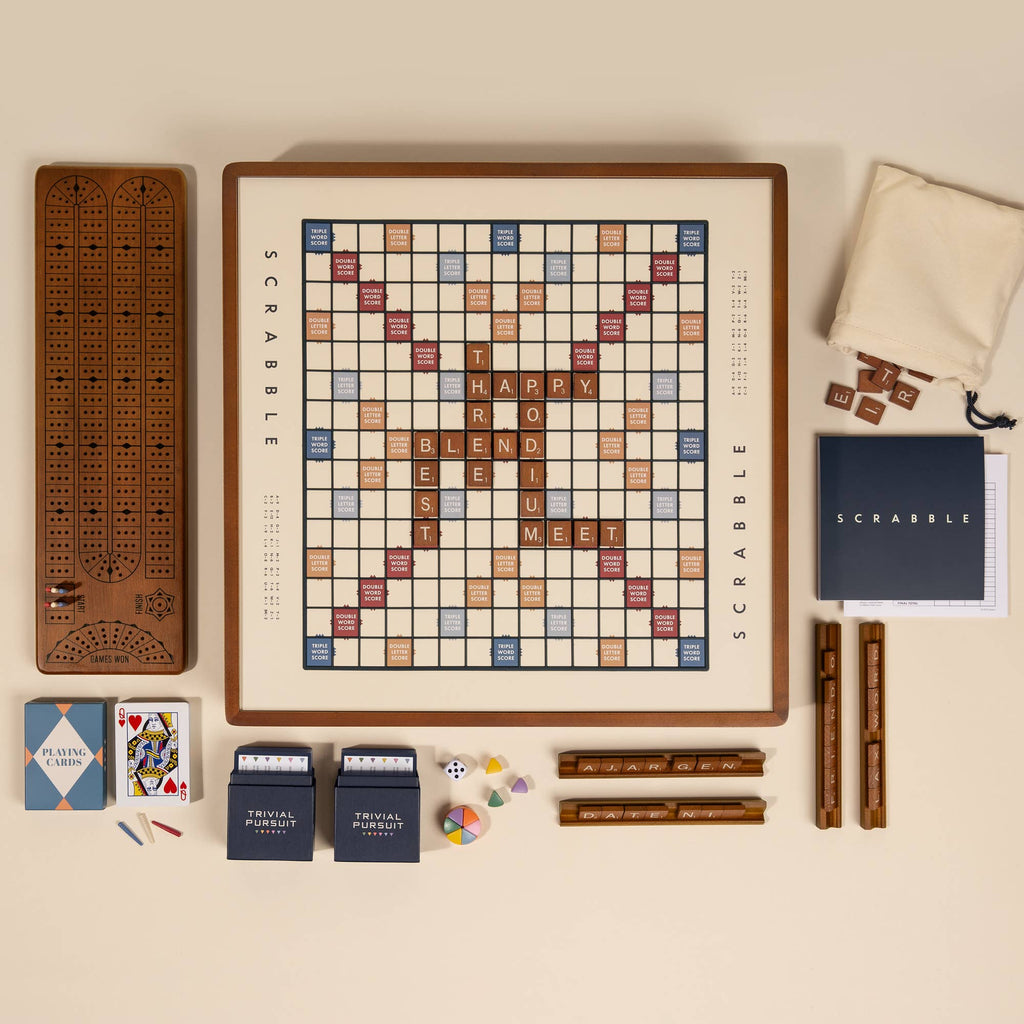 The 3-in-1 Game Collection features a Scrabble board with letter tiles and racks, Trivial Pursuit cards, playing cards, dice, colored tokens, and a classic wooden cribbage board—all the essentials for game night.
