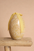 The Maileg Easter Egg, Medium - Cream Yellow, featuring a pale yellow floral pattern and a yellow ribbon bow, sits on a rustic wooden stool against a beige background.