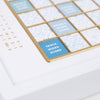 Close-up of a Scrabble Bianco Edition game board with a blue and white patterned grid, gold edges, and labeled squares including “Double Word Score” and “Triple Word Score.”