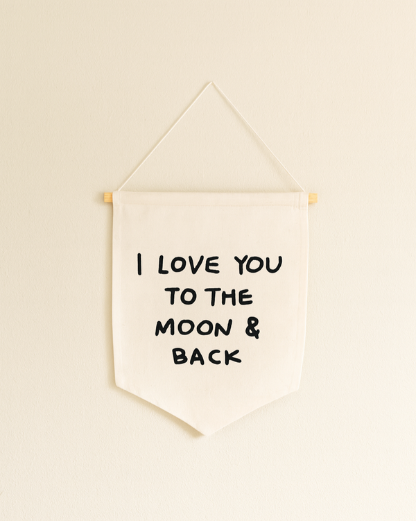 The I Love You To The Moon And Back Canvas Sign is a white fabric wall banner on a wooden dowel with bold black lettering—ideal handmade wall decor or artisan gift.
