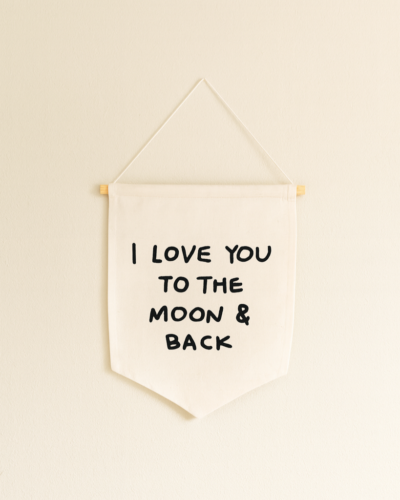 The I Love You To The Moon And Back Canvas Sign is a white fabric wall banner on a wooden dowel with bold black lettering—ideal handmade wall decor or artisan gift.