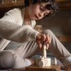 A young child with curly hair and a knit sweater carefully places an Ostheimer figure from the Hello Winter Set (Grapat X Ostheimer Limited Edition) onto a spinning top on the table.