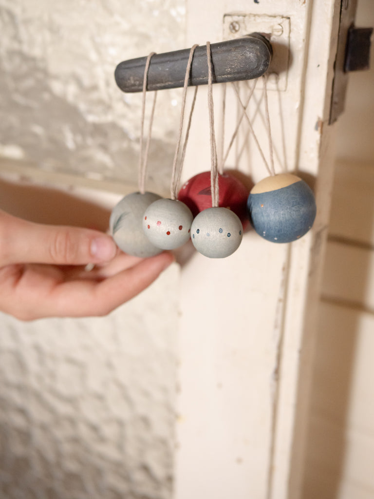 A hand touches a set of Grapat Ornament Set - Wish Balls, pastel-colored festive decorations tied with string and hanging from a black handle on a white textured door.