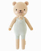 Cuddle + Kind Alexander The Honey Bear is a soft, knitted handmade teddy bear in light green overalls with a tiny bear in its pocket, filled with hypoallergenic polyfill and shown on a plain white background.