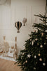 A decorated Christmas tree with white and gold ornaments stands by presents and wooden decorations; two Hot Air Balloon - Black handmade decorations hang above, perfect for adding festive charm to a children's room.
