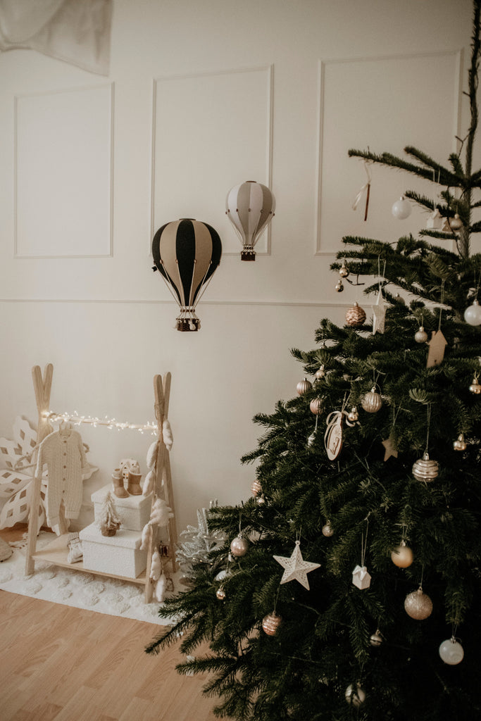 A decorated Christmas tree with white and gold ornaments stands by presents and wooden decorations; two Hot Air Balloon - Black handmade decorations hang above, perfect for adding festive charm to a children's room.