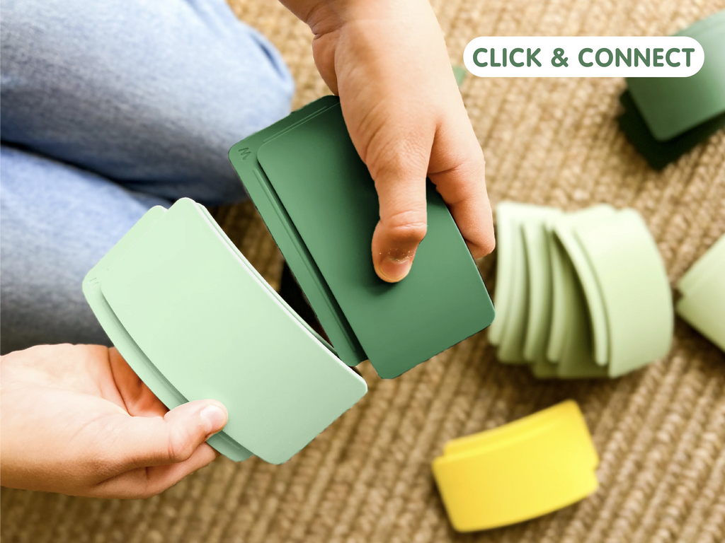 A person holds two green plastic arches from the WaytoPlay: Arches - Starter Set, connecting them while additional arches rest on the carpet. Text in the corner reads, “CLICK & CONNECT.”.