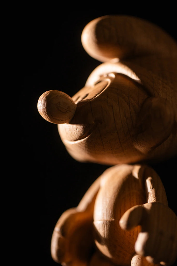 In a dimly lit setting, a wooden statue called "Smurf, Oak" depicts a cartoon mouse with large ears and distinctive nose, boasting smooth carving and intricate details reminiscent of Smurf Village craftsmanship.