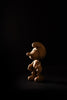 The Smurf, Oak figurine, a small wooden character resembling those from Smurf Village, stands illuminated against a dark background. Its hat and large shoes cast a subtle shadow that hints at Gargamel lurking nearby.