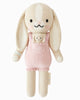 Cuddle + Kind Briar The Bunny - Peony Pink is a hand-knit, fair trade bunny doll with long floppy ears, pink overalls, a small matching bunny in the pocket, embroidered details, and a soft plush design.