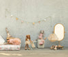 A pastel children's room features three Maileg Bunny, Size 2 - Classic - Ballet Suit and Skirt - Rose dolls, a gold-framed mirror, ballet slippers, and a garland on a light textured wall.