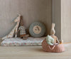 The Maileg Rabbit, Size 3 - Brown, dressed in a shirt and shorts, is arranged with other stuffed animal toys on a floral cushion beside a round mountain pillow. The rabbit sits in a pink basket with small plush toys.