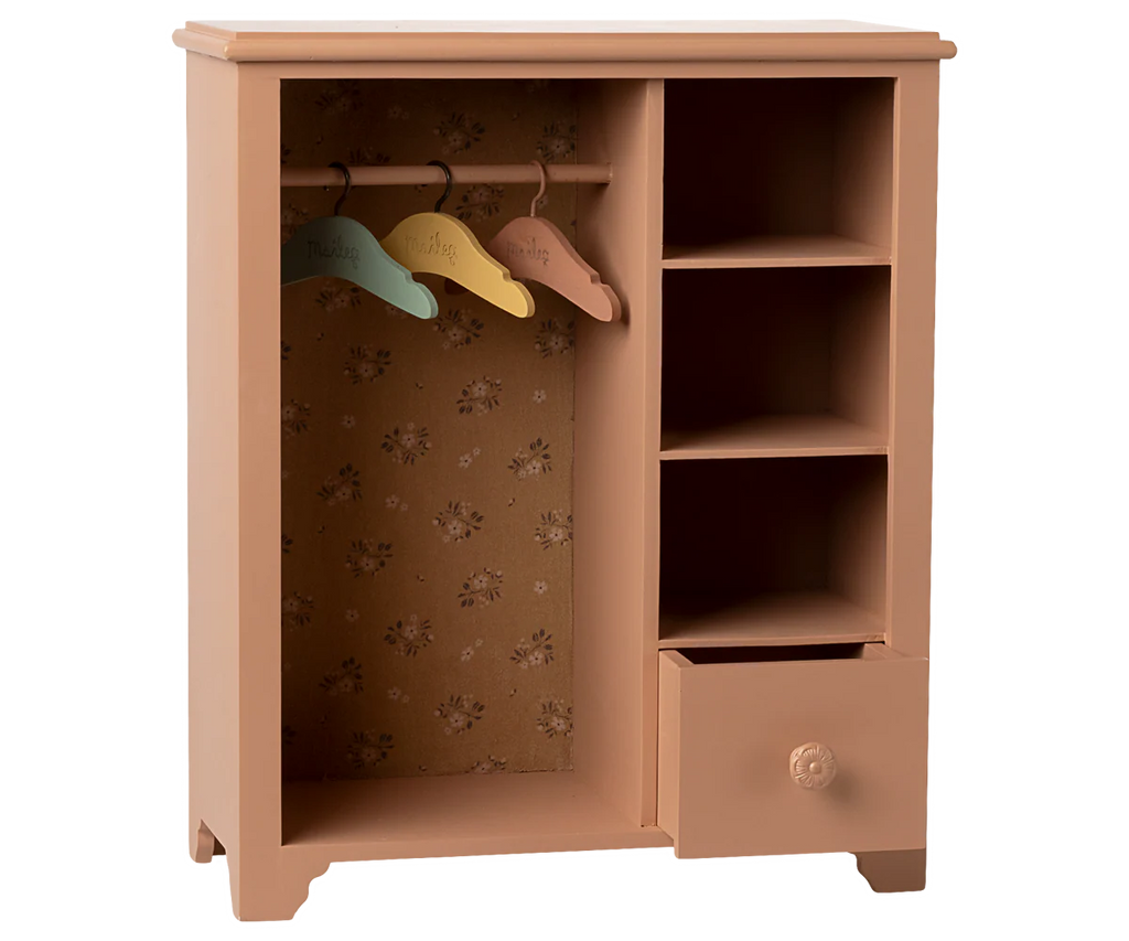 The Maileg Wardrobe, Large - Dark Powder features a pink wooden design with floral backing, three pastel hangers for doll clothes, four right-side shelves, and an open bottom drawer—ideal for organizing a child's room.