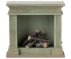 The PRE-ORDER: Fireplace, Miniature - Dusty Green (ships early October) is a small, rustic green-painted wooden fireplace with a vintage finish and short round firewood logs stacked inside the open firebox.