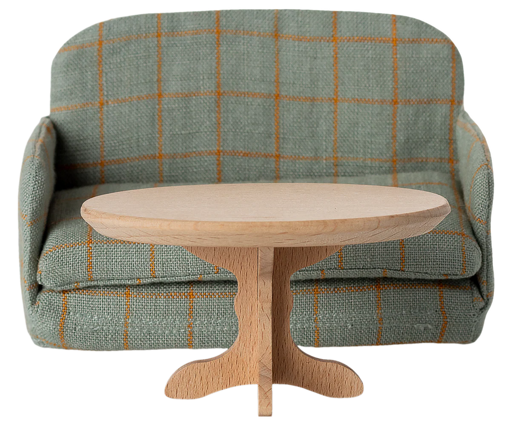 A small, oval wooden PRE-ORDER: Oval Coffee Table, Mouse - Nature (Estimated Ship Date: Early October) sits in front of a green plaid-patterned miniature sofa—perfectly mouse-sized, making for charming SuitCasa dollhouse furniture.