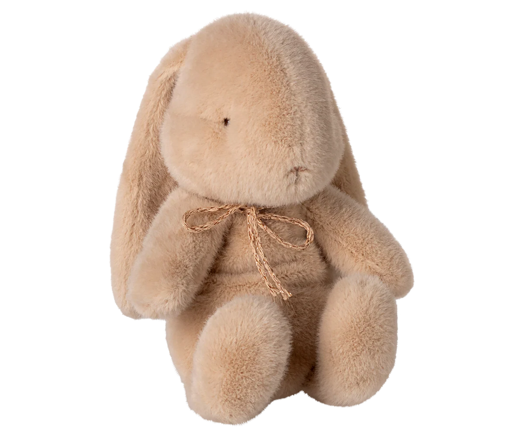 The Maileg Plush Bunny, Small - Latte is a soft light brown stuffed animal with floppy ears, simple stitched eyes and nose, and a small bow around its neck, shown sitting upright against a plain white background.
