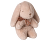 The Maileg Plush Bunny, Mini - Light Powder, is a soft stuffed animal in light powder recycled polyester, featuring floppy ears, simple stitched facial features, and a brown ribbon bow around its neck. It sits upright against a white background.