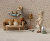 Two mice tidy their Mouse hole Farmhouse: one hangs laundry above the Maileg Couch, Mouse Size - Mable, while the other vacuums near a tea set in a vintage room with floral wallpaper and a lamp.