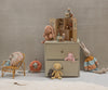 A nursery scene with plush toys, a dollhouse, and a rattan chair. Safari friends, including the Maileg Gorilla, Mini, a bunny in a striped sweater and a plush bear sit by the gray dresser on the soft fabric rug.