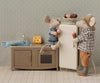 Two toy mice in a miniature kitchen, one dressed in Maileg Extra Clothing: Jacket, Pants, Hat and Bow Tie for Grandpa Mouse, enjoy ice cream with fridge, cheese, fish, patterned wallpaper, and charming doll clothing details.