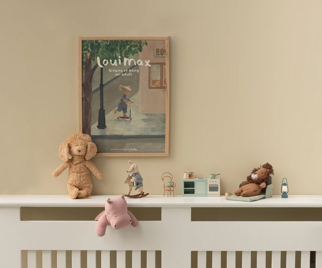 A nursery shelf displays soft fabric plush toys, a Maileg Lion, Mini from the safari friends collection, a miniature kitchen set, and small figurines. Above, a framed illustration shows "louimax Dreams of Being an Adult.