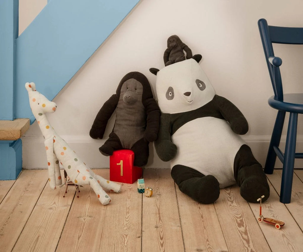 Three safari friends—a giraffe with colorful dots, a Maileg Gorilla (Medium), and a large soft panda—sit on a wooden floor by a blue chair and staircase, with small toy cars and a red block numbered 1 nearby.
