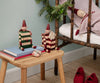 A PRE-ORDER Maileg Elf with Drawer - Red (Estimated Arrival Mid August) sits near books and a festive gift box, while a doll on a rustic chair and holiday décor like pine greenery and red shoes complete the charming scene.
