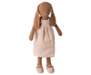 The Maileg Bunny, Size 3, in chocolate brown stands upright in a light pink dress and matching shoes against a white background.