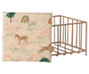 A square cushion with a whimsical horse, rainbow, and tree design sits next to the Maileg Playpen, Micro - Dark powder (arriving 02/15/26), creating a charming accent for your nursery or play area.