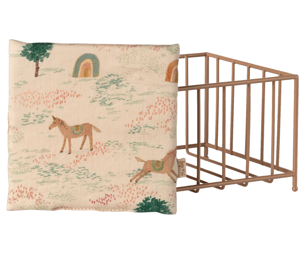 A square cushion with a whimsical horse, rainbow, and tree design sits next to the Maileg Playpen, Micro - Dark powder (arriving 02/15/26), creating a charming accent for your nursery or play area.