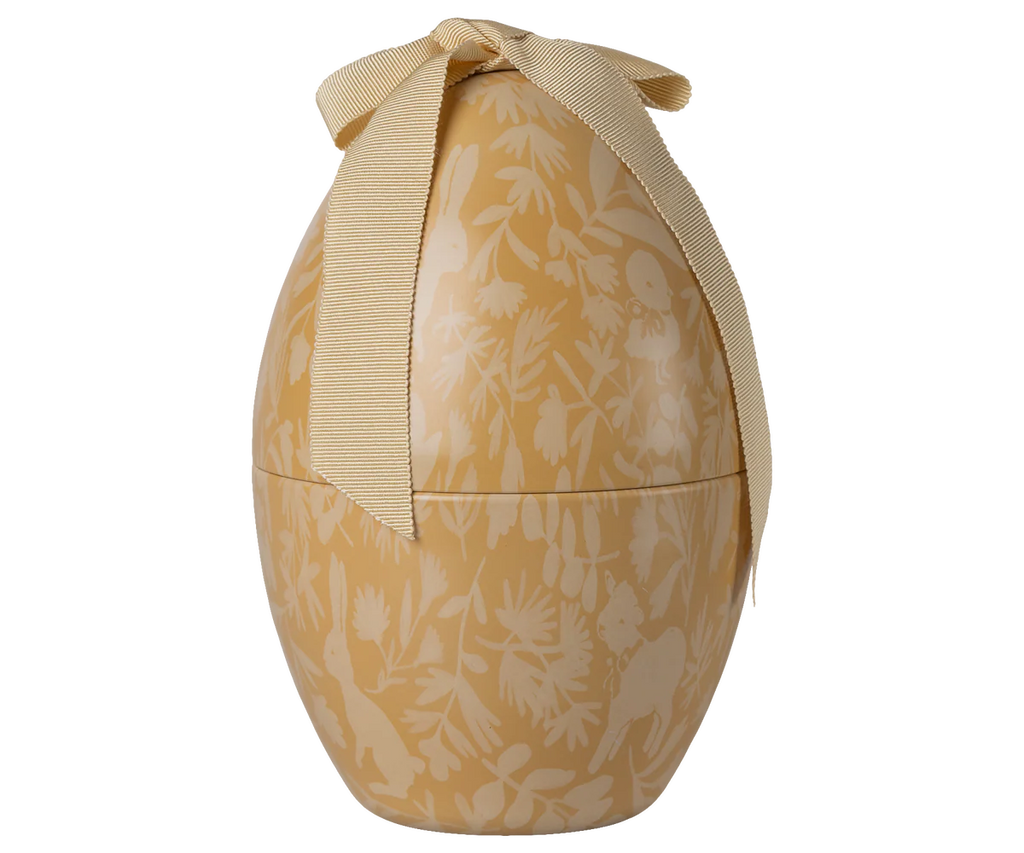 The Maileg Easter Egg, Medium - Cream Yellow, is a decorative metal egg-shaped container with a beige and cream floral pattern and a large beige ribbon bow—perfect for any festive display.