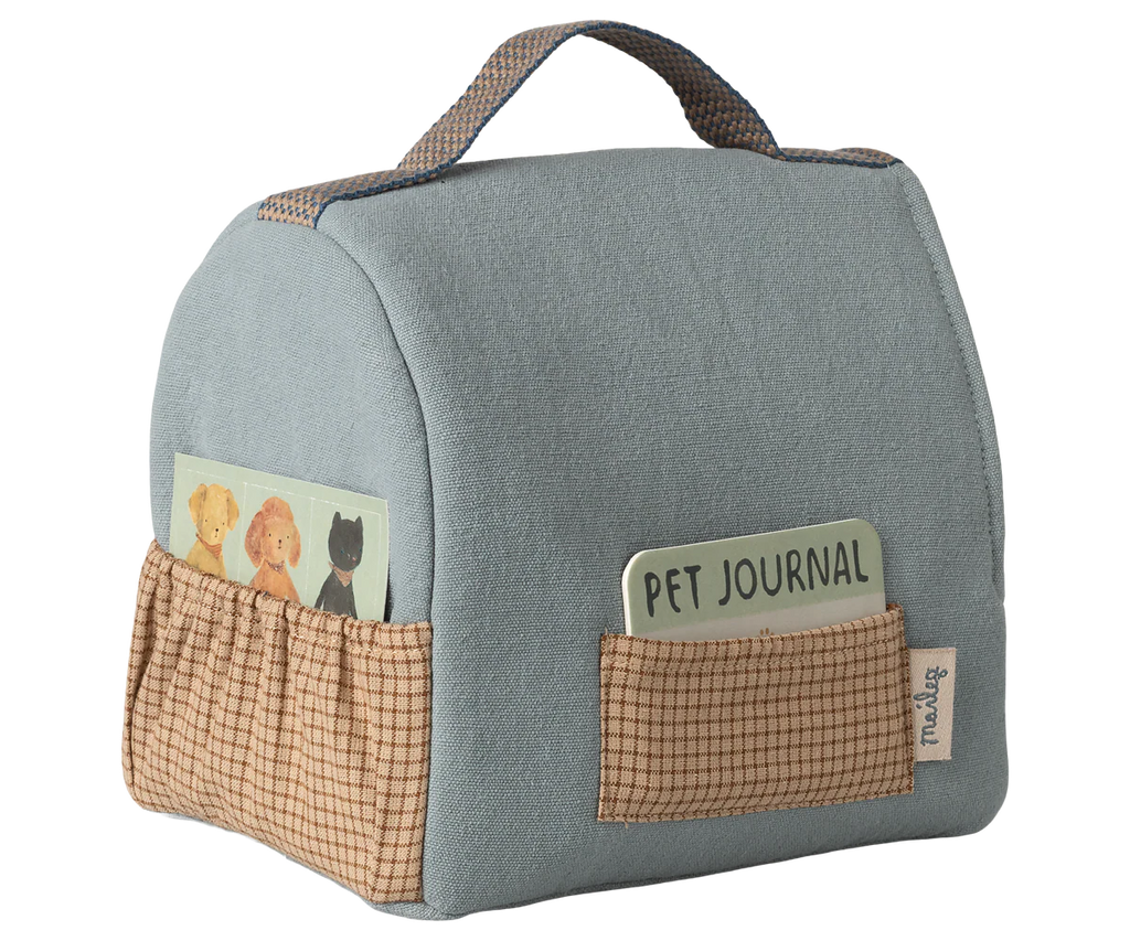 The Maileg Pet Carrier - Dusty Blue features plaid brown pockets, a card with pet illustrations, a "Pet Journal" tag, and a top handle for easy carrying—perfect for organizing pet accessories.
