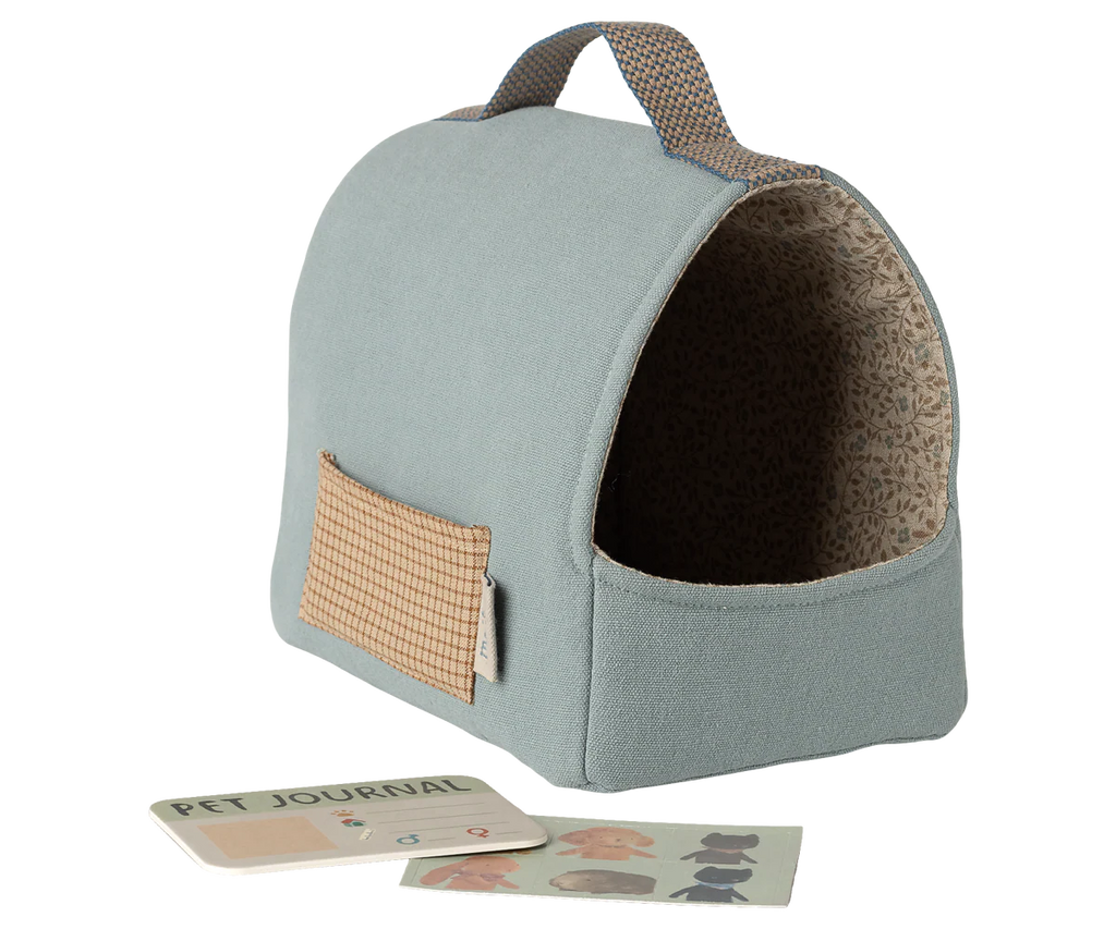 The Maileg Pet Carrier - Dusty Blue (arriving 02/15/26) is a small fabric carrier with a brown handle and patterned trim, shown with a "Pet Journal" and two illustrated cards—ideal for carrying your soft puppy and pet accessories.