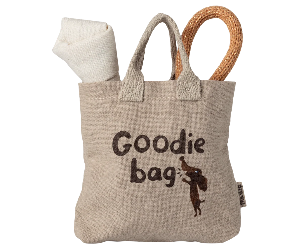 The Maileg Pet Supply, Toys: A beige tote bag with “Goodie bag” and a cartoon dog print, ideal for puppy accessories or a magnetic puppy bone, with a rolled white cloth and textured tan loop handle (arriving 03/15/26).