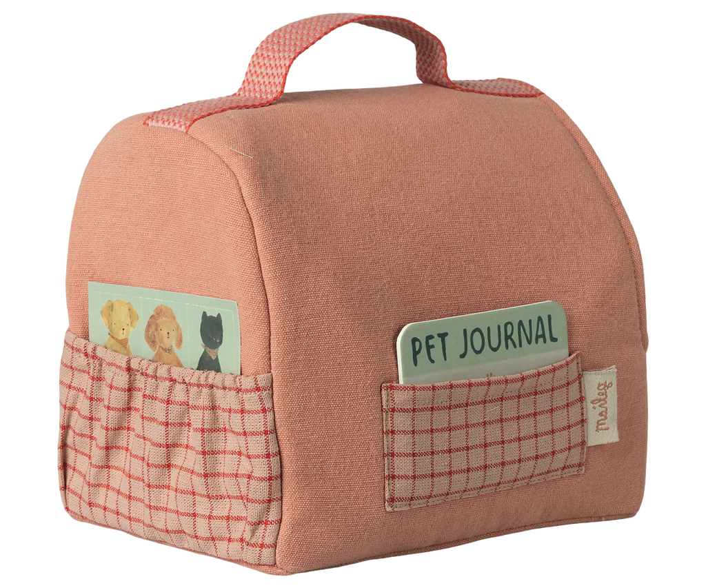 The Maileg Pet Carrier - Coral is a soft pink carrier with a handle, red checkered pocket, and two visible cards—one labeled "Pet Journal" and one with animal illustrations. Ideal for pet accessories. Pocket tag reads "maileg." Arriving 02/15/26.