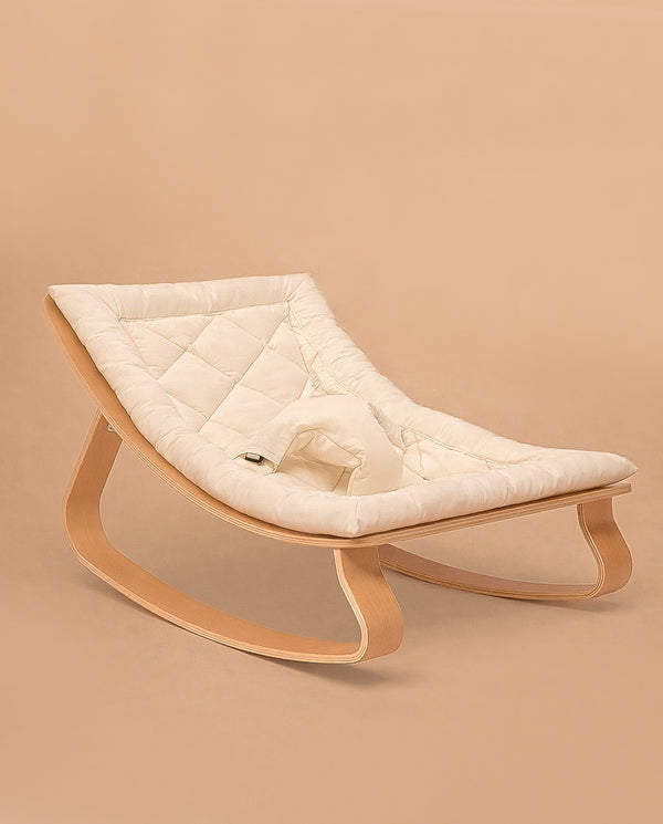 The Charlie Crane LEVO Baby Rocker features a light wooden frame and a soft, quilted organic white cushion, shown against a neutral beige background.