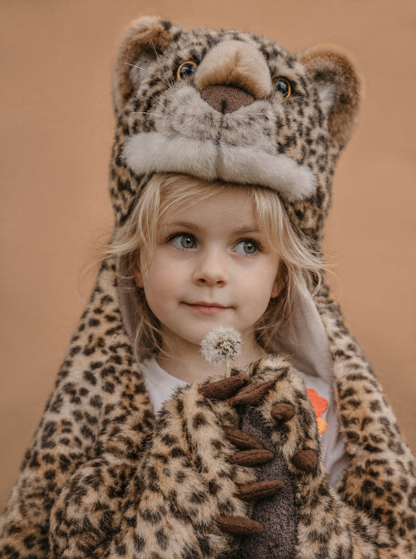 A young child dressed in the Costume - Leopard, featuring a faux fur leopard print with hood and paws, stands against a plain brown background holding a dandelion—an adorable and unique kids gift idea.