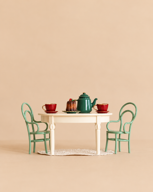 A Maileg Christmas Tea Set featuring a miniature vintage dining table, two green chairs, two red cups, a green teapot, and a small bundt cake.